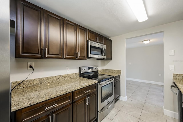 kitchen featuring light stone countertops, light tile patterned floors, stainless steel appliances, and dark brown cabinets