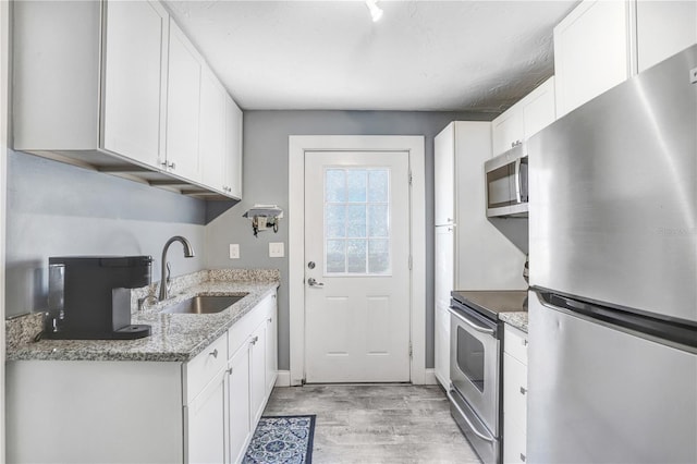 kitchen featuring stainless steel appliances, sink, stone countertops, light hardwood / wood-style flooring, and white cabinetry