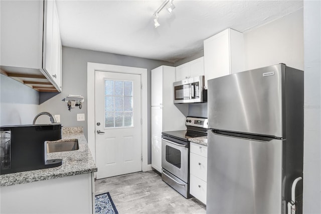 kitchen featuring appliances with stainless steel finishes, track lighting, light stone counters, white cabinets, and light hardwood / wood-style floors