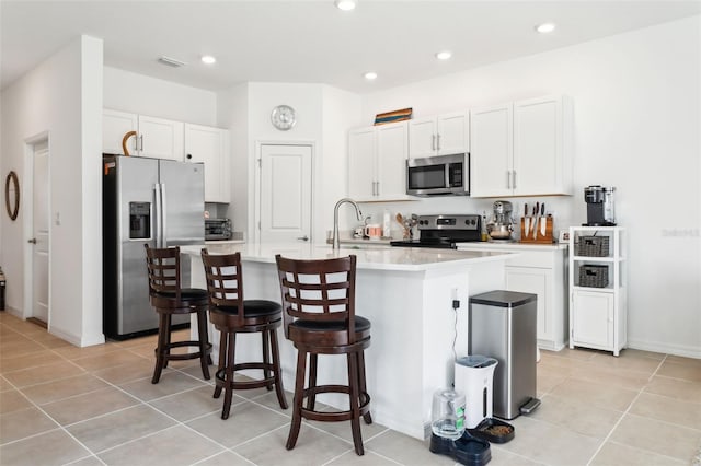 kitchen with a breakfast bar area, a kitchen island with sink, a sink, light countertops, and appliances with stainless steel finishes