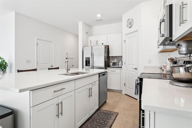 kitchen with stainless steel appliances, sink, an island with sink, white cabinetry, and light tile patterned flooring