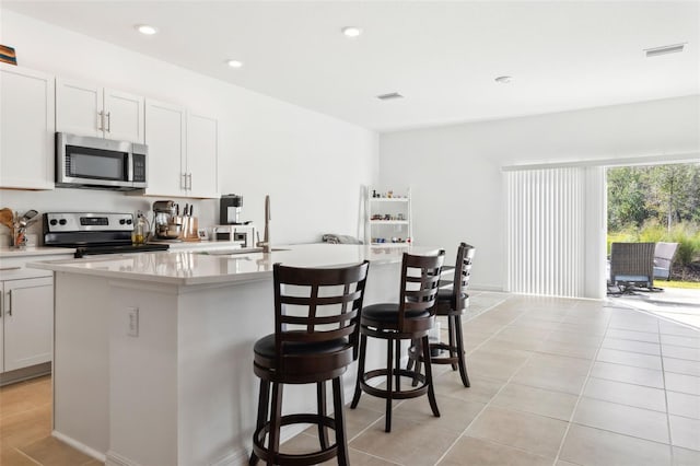 kitchen with an island with sink, a sink, a kitchen breakfast bar, appliances with stainless steel finishes, and light countertops