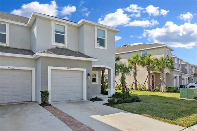 view of property featuring driveway, a front yard, stucco siding, an attached garage, and a residential view