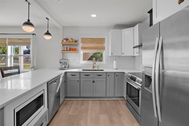 kitchen with kitchen peninsula, decorative light fixtures, gray cabinets, appliances with stainless steel finishes, and sink