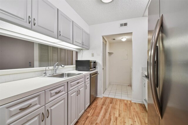 kitchen featuring gray cabinetry, sink, a textured ceiling, appliances with stainless steel finishes, and light hardwood / wood-style floors