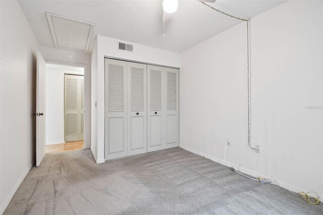 unfurnished bedroom featuring a textured ceiling, ceiling fan, light carpet, and a closet