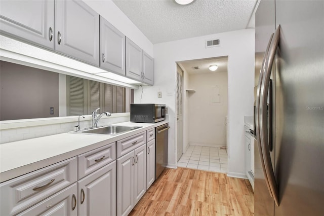 kitchen featuring sink, a textured ceiling, gray cabinets, stainless steel appliances, and light hardwood / wood-style floors