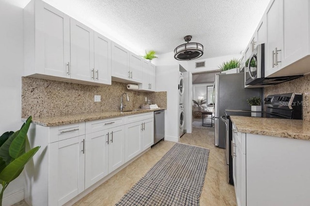 kitchen featuring stainless steel appliances, white cabinetry, and stacked washer / dryer