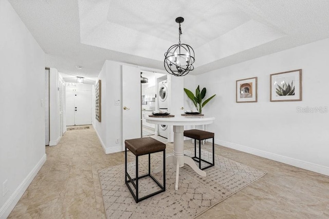 office with stacked washer and dryer, a textured ceiling, a tray ceiling, and an inviting chandelier