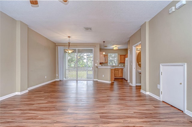 unfurnished living room with light wood-type flooring and a textured ceiling