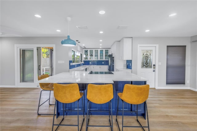 kitchen with white cabinets, hanging light fixtures, fridge, light stone counters, and kitchen peninsula