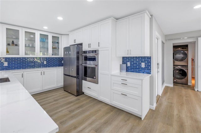 kitchen featuring stacked washing maching and dryer, white cabinets, stainless steel appliances, and light stone counters