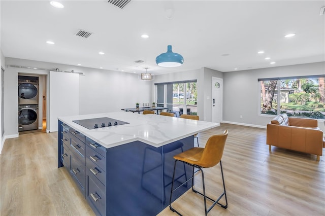 kitchen with pendant lighting, light stone countertops, black electric cooktop, stacked washer / drying machine, and light hardwood / wood-style floors