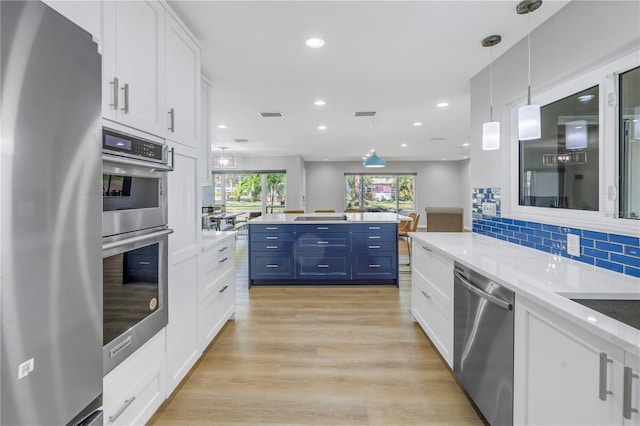 kitchen with decorative backsplash, appliances with stainless steel finishes, blue cabinetry, white cabinets, and hanging light fixtures