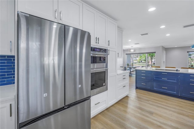 kitchen with blue cabinetry, white cabinets, stainless steel appliances, and light hardwood / wood-style floors