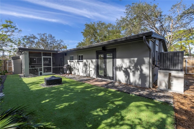 back of house featuring a sunroom, a yard, cooling unit, and an outdoor fire pit