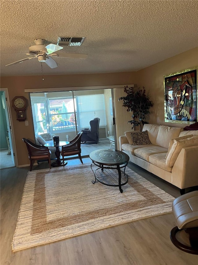 living room featuring ceiling fan, wood-type flooring, and a textured ceiling