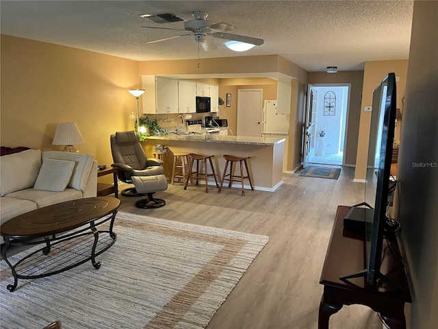 living room with ceiling fan, sink, a textured ceiling, and light hardwood / wood-style flooring