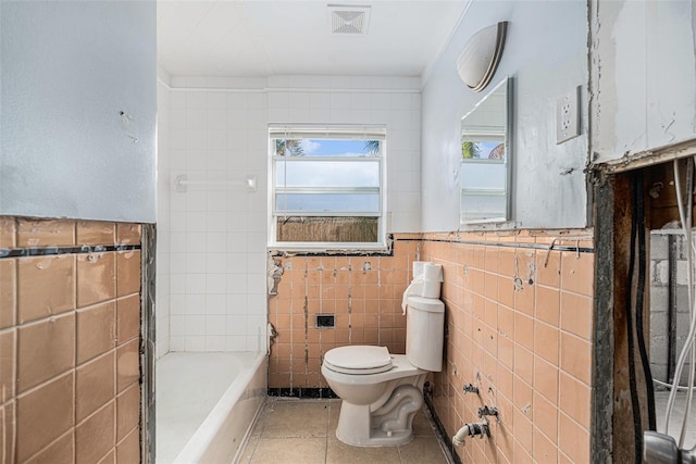 bathroom with a bathing tub, tile patterned flooring, tile walls, and toilet