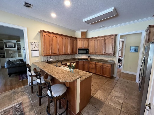 kitchen featuring a kitchen breakfast bar, sink, stainless steel fridge, ornamental molding, and a textured ceiling