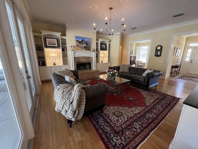 living room with a tile fireplace, ornamental molding, light hardwood / wood-style floors, and a notable chandelier