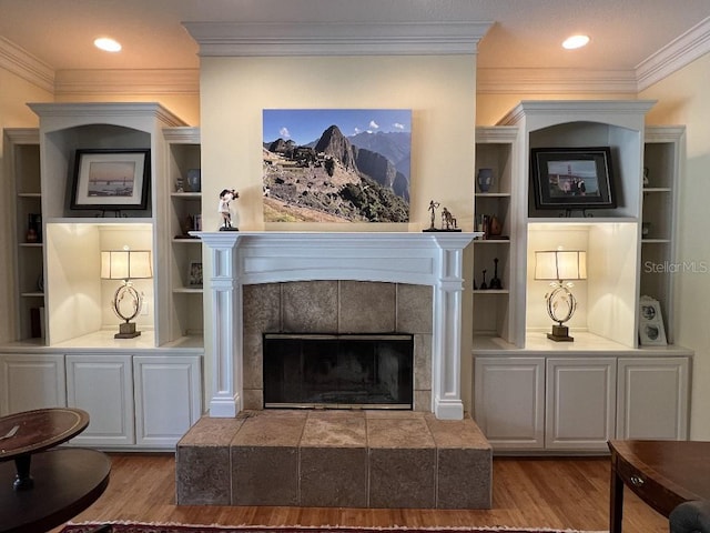 living room with a tile fireplace, built in shelves, and wood-type flooring