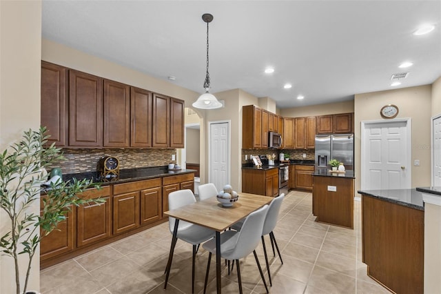 kitchen with appliances with stainless steel finishes, backsplash, light tile patterned floors, decorative light fixtures, and a center island