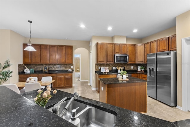 kitchen with sink, a kitchen island, decorative light fixtures, light tile patterned floors, and appliances with stainless steel finishes