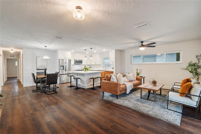 living room with dark hardwood / wood-style flooring, ceiling fan with notable chandelier, a textured ceiling, and sink