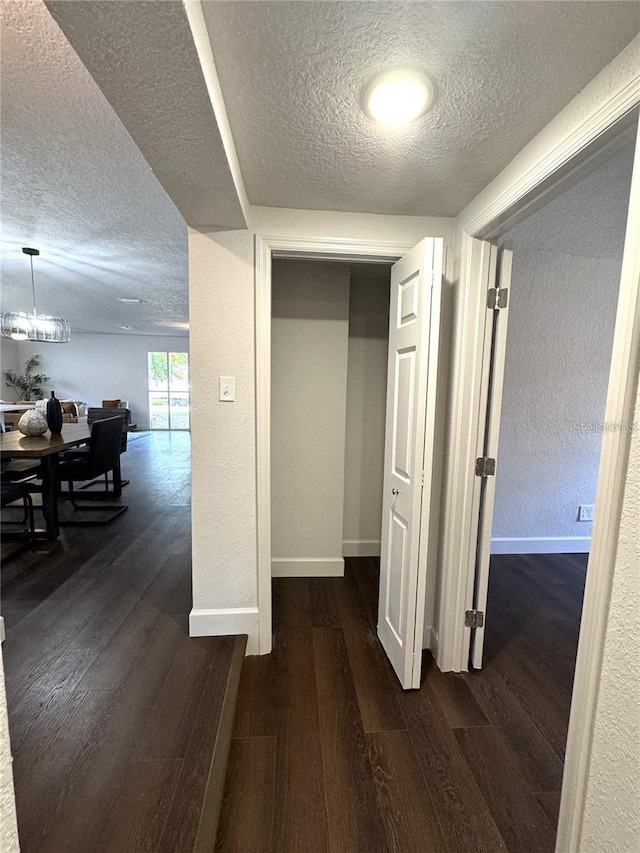 corridor featuring a textured ceiling, a chandelier, and dark hardwood / wood-style floors