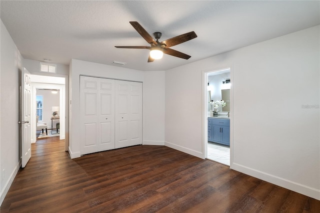 unfurnished bedroom with a textured ceiling, ceiling fan, connected bathroom, dark hardwood / wood-style floors, and a closet