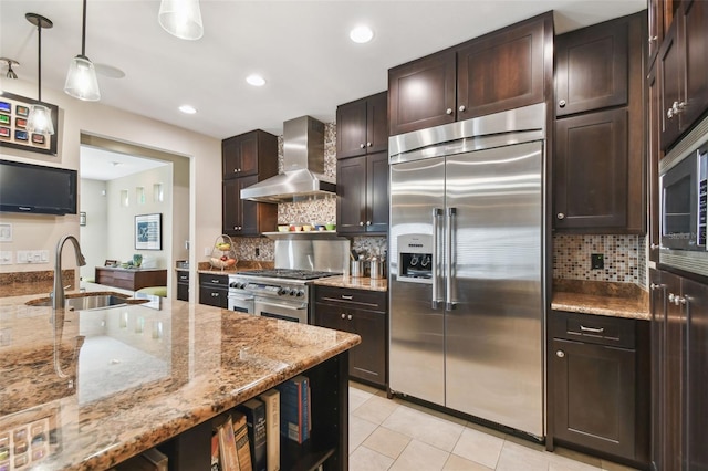 kitchen with decorative light fixtures, wall chimney range hood, sink, backsplash, and high quality appliances