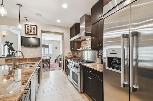 kitchen featuring premium appliances, pendant lighting, wall chimney exhaust hood, light stone counters, and sink