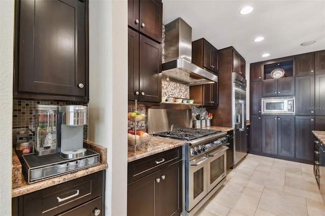 kitchen featuring dark brown cabinets, tasteful backsplash, built in appliances, and wall chimney range hood