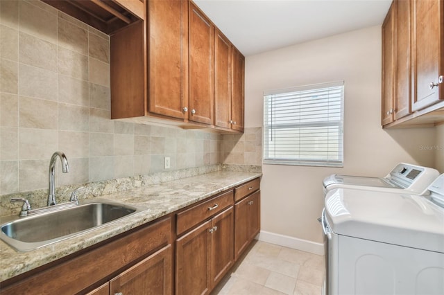 clothes washing area with sink, light tile patterned flooring, washer and dryer, and cabinets