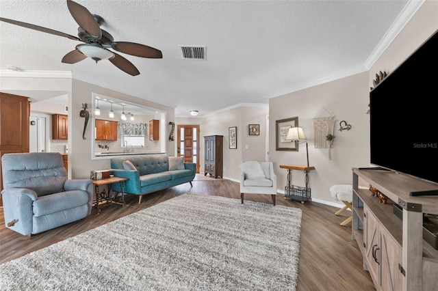 living room with ceiling fan, dark wood-type flooring, a textured ceiling, and ornamental molding