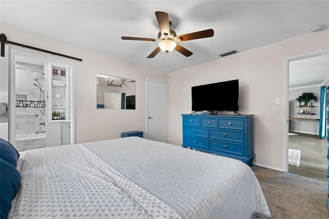 bedroom featuring dark carpet, a textured ceiling, ceiling fan, a barn door, and connected bathroom