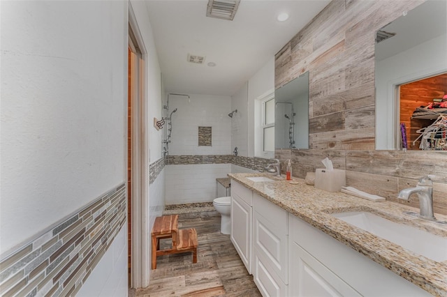 bathroom featuring tiled shower, vanity, toilet, and tile walls