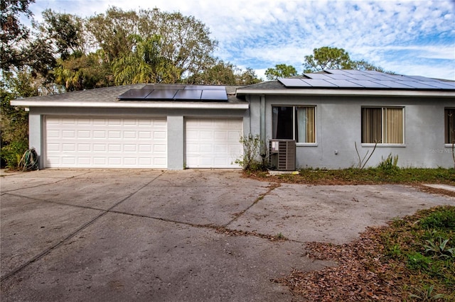 view of front of home with central AC unit, solar panels, and a garage