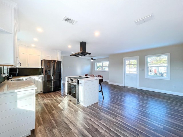 kitchen with a kitchen island, refrigerator with ice dispenser, stainless steel range with electric cooktop, island range hood, and white cabinets