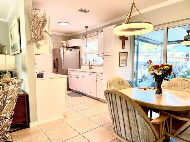 kitchen featuring white dishwasher, crown molding, light tile patterned floors, decorative light fixtures, and white cabinetry