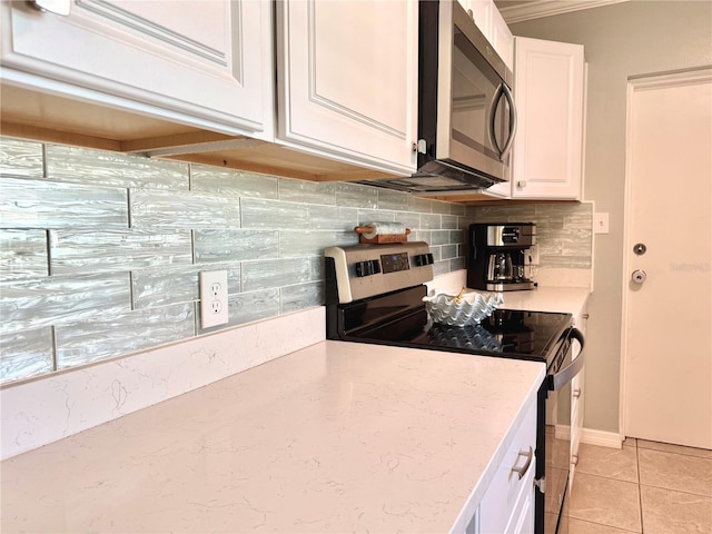 kitchen with light tile patterned floors, appliances with stainless steel finishes, decorative backsplash, white cabinets, and ornamental molding