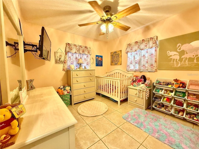 bedroom with ceiling fan, tile patterned flooring, and a crib