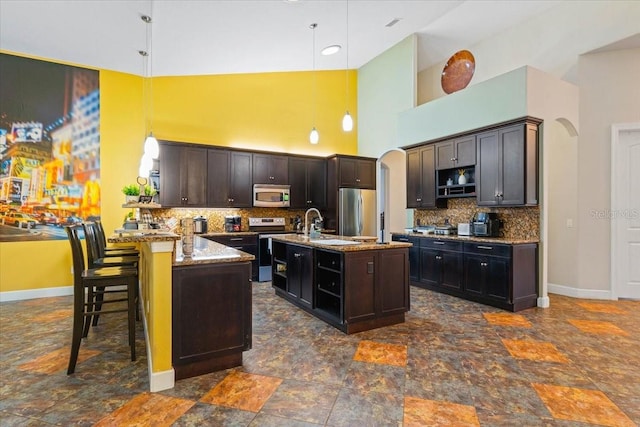 kitchen featuring a breakfast bar, decorative light fixtures, stainless steel appliances, and an island with sink