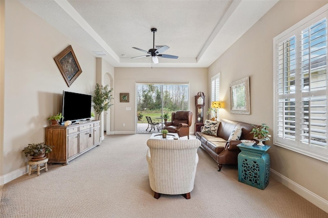 carpeted living room with ceiling fan and a raised ceiling