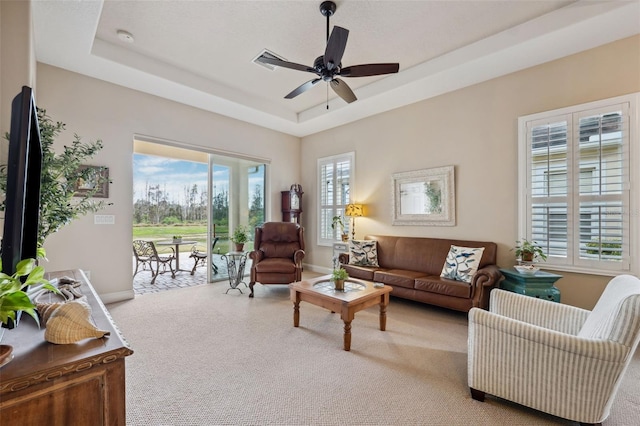 living room featuring light carpet, a tray ceiling, and ceiling fan