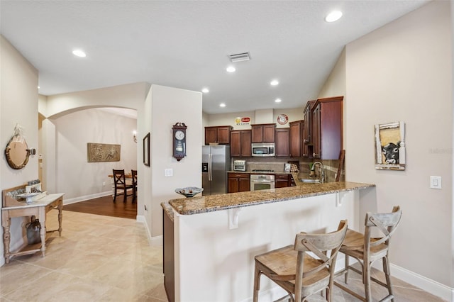 kitchen with kitchen peninsula, appliances with stainless steel finishes, a kitchen breakfast bar, sink, and stone counters