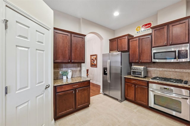 kitchen featuring tasteful backsplash, light stone counters, and appliances with stainless steel finishes