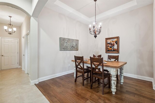 dining space featuring a raised ceiling, hardwood / wood-style floors, and an inviting chandelier