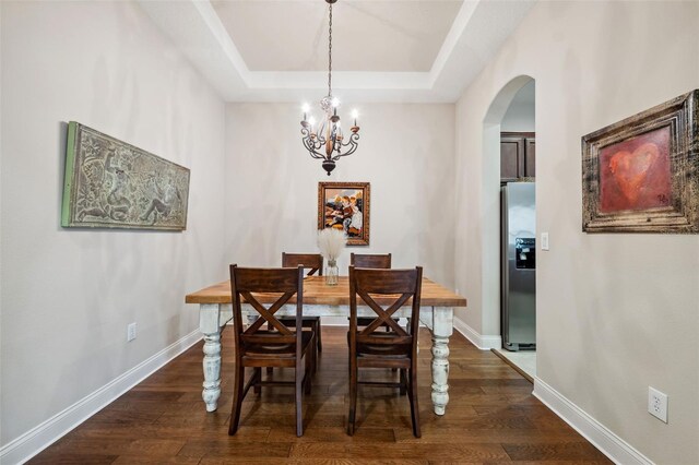 dining space with a raised ceiling, dark wood-type flooring, and an inviting chandelier